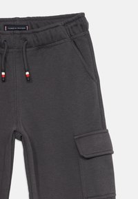 Mörkgrå cargojoggingbyxor med elastisk midja, dragsnören med röda, vita och svarta spetsar, sidofickor och en fackficka på låret.