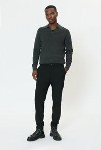 Pilkas megztas megztinis su šaliko apykakle, derinamas su juodomis trumpintomis kelnėmis ir juodais bateliais su raišteliais; lygus audinys ir prigludęs dizainas.