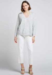 Pull-over gris clair en v avec une coupe ample, associé à un pantalon blanc cropped orné de petites broderies de fleurs jaunes et des talons beiges.