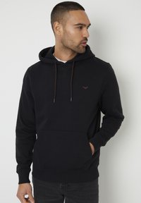 Hoodie noir en tissu doux, avec une poche avant, des cordons de serrage ajustables et un petit logo sur la poitrine. Design chaud et décontracté.