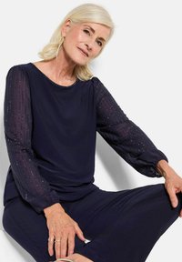 Top navy con maniche trasparenti e testurizzate con piccoli dettagli decorativi, scollo rotondo e vestibilità comoda; abbinato a pantaloni coordinati.