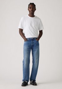 Witte t-shirt met korte mouwen, vervaagde blauwe rechte spijkerbroek en zwarte schoenen. Eenvoudig ontwerp, lichte stof en klassieke denimtextuur.