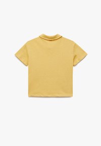 Camisa polo amarilla de manga corta con cuello, confeccionada en tela texturizada, con un diseño simple y minimalista.