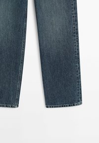 Jean en denim bleu foncé avec une coupe décontractée, des jambes droites et un design classique à cinq poches. Présente un léger délavage et des surpiqûres blanches.