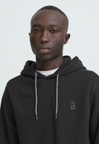 Zwarte hooded sweatshirt van een gestructureerde stof, met een contrasterende grijze trekkoord en een klein logo op de borst.