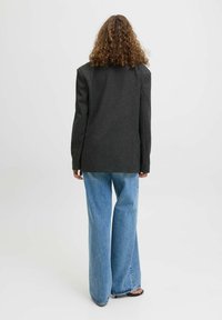 Černý blazer ze směsi vlny se strukturovaným střihem, otevřeným zadním dílem a dlouhými rukávy, doplněný širokými světle modrými džíny.