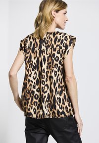 Leoprint-Oberteil mit kurzen Ärmeln, entspanntem Schnitt, glattem Stoff und schwarzen Akzenten auf der Rückseite. Getragen mit schwarzen Hosen.