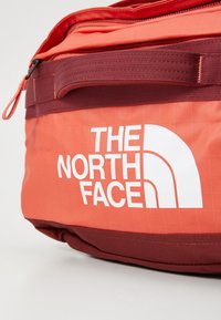 Red and maroon The North Face bag with a zipper and carrying handle on a plain white background.