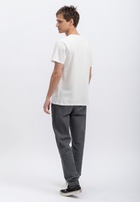 Witte katoenen t-shirt met korte mouwen, gecombineerd met grijze broek met een turquoise accent. Model draagt zwarte sneakers.