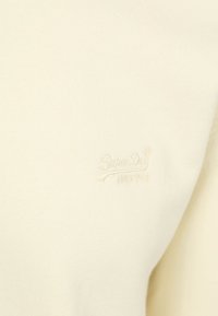 Cream-colored sweatshirt made of soft fabric, featuring an embroidered "SuperDry" logo on the left side. Simple and minimalistic design.