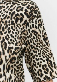 Leopardprint stof med sorte pletter på en beige baggrund; struktureret overflade; korte ærmer med en bølget kant.