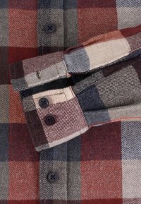Koszula flanelowa w czerwono-niebiesko-kremową kratę. Posiada zapięcie na guzik przy mankietach z ciemnymi guzikami, miękką teksturę oraz złożony kołnierz.