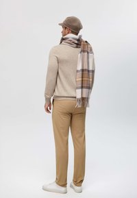 Maglione beige, pantaloni color cammello e sneakers bianche. Avvolto in una sciarpa a scacchi nei colori beige, marrone e crema. Un cappello di lana completa il look.