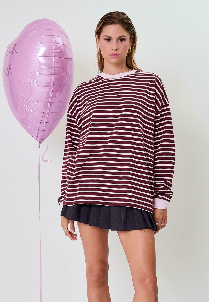 Bordovai ir baltai dryžuota ilgomis rankovėmis marškinėliai su apvalia iškirpte, poruojami su tamsiai raukšlėta sijonu. Šalia yra rožinis širdelės formos balionas.