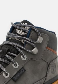 Szare zamszowe buty trekkingowe z teksturowanym materiałem, wzorzystymi sznurówkami, metalowymi oczkami i logo Timberland, wyposażone w gumową podeszwę oraz wyprofilowany kołnierz.