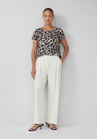 Blouse à manches courtes en imprimé léopard associée à un pantalon blanc taille haute et des sandales à talons noires. Tissu lisse, coupe décontractée et look casual.