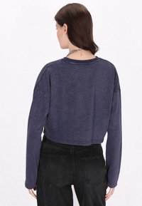 Przycięty granatowy top z długim rękawem, wykonany z lekkiego materiału, o luźnym kroju. Posiada okrągły dekolt i opadające ramiona.