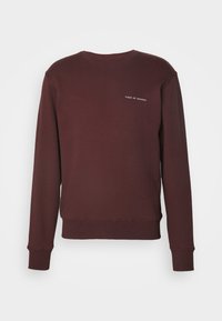 Felpa crewneck bordeaux con maniche lunghe e piccolo logo testuale bianco "Tiger of Sweden" sul petto sinistro.