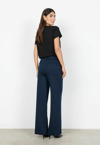 Marineblauwe brede broek met een gladde textuur, met twee achterzakken. Gecombineerd met een aansluitende zwarte top met korte mouwen.