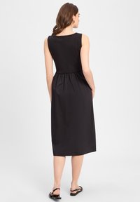 Schwarzes ärmelloses Kleid mit einem taillierten Oberteil, gerafftem Taillenbereich und knielanger Rocklänge. Weiche Textur und schlichtes Design.