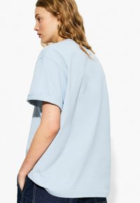 T-shirt di cotone azzurro chiaro con maniche corte, vestibilità comoda e risvolti, vista di lato con una texture liscia e un design semplice.