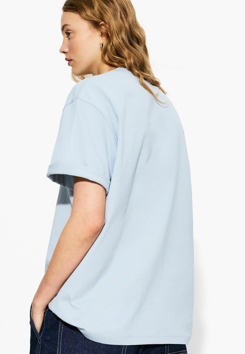 T-shirt di cotone azzurro chiaro con maniche corte, vestibilità comoda e risvolti, vista di lato con una texture liscia e un design semplice.