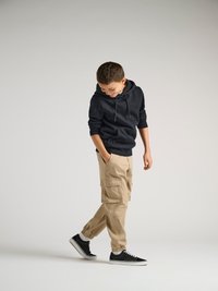 Svart hettegenser, beige cargo-bukser med lommer og svarte sneakers med hvite såler. Glatt stoff, avslappet passform og avsmalnende ermer.