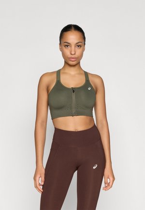 Olivengrøn sport BH med lynlås foran, brede stropper og åndbare perforeringer. Sammen med højtaljede brune leggings med sidelommer.