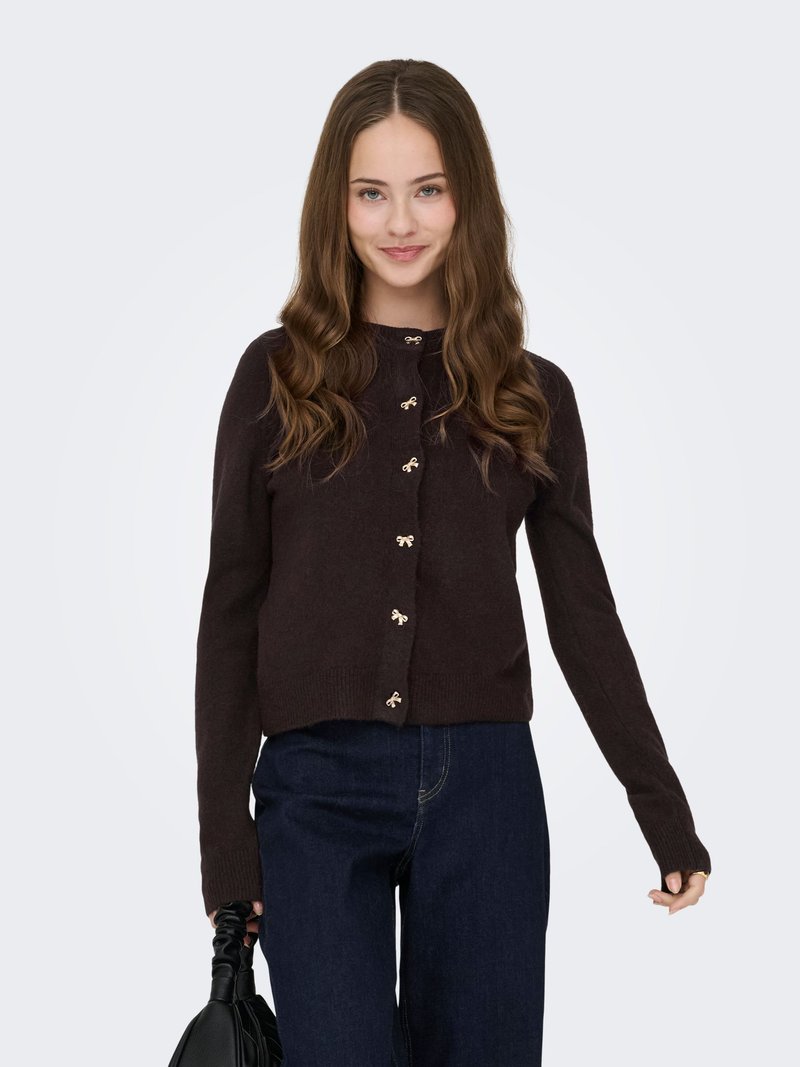 Braune gestrickte Strickjacke mit rundem Ausschnitt, ausgestattet mit goldfarbenen dekorativen Knöpfen, langen Ärmeln und einer kurzen Passform, kombiniert mit dunklen Jeans.