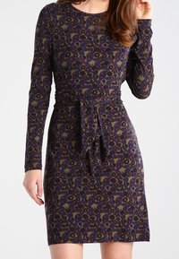 Długo rękawowa, dopasowana sukienka w ciemnofioletowym kolorze z kwiatowym nadrukiem w zieleni i żółci. Posiada paskiem do wiązania w talii oraz okrągły dekolt.