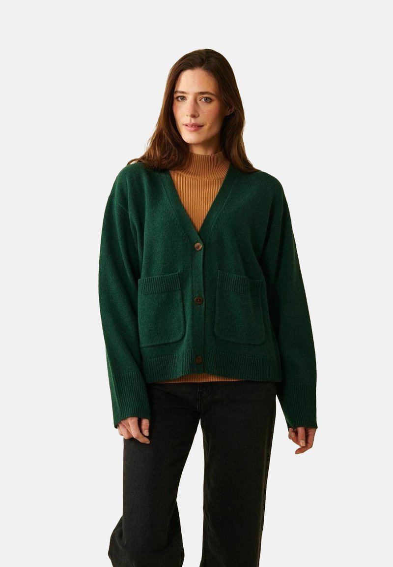 Grön stickad kofta med V-hals, tre knappar och två framfickor. Strukturerad tyg och lös passform, lagrad över en ribbad brun polotröja.