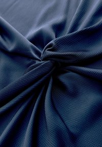 Merevam sinisel tekstuuril kangal on sõlme keeratud, rõhutades kootud mustrit ja voltimist.