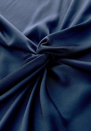 Marineblauer, strukturierter Stoff, zu einem Knoten verdreht, der das gewebte Muster und die Falten hervorhebt.