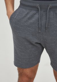 Grå shorts med et struktureret mønster, der har tynde hvide linjer, en ribbet talje og snorelukning. Lomme på siden synlige.