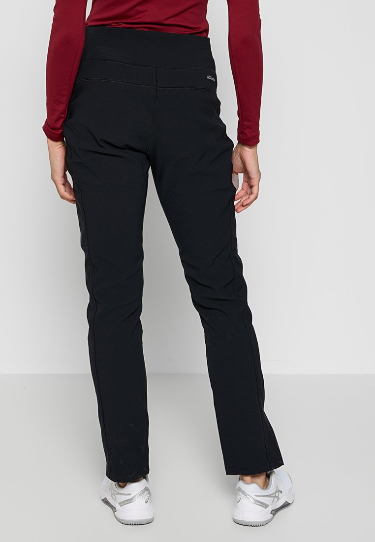 Czarne spodnie sportowe o gładkiej fakturze, dopasowanym kroju i wysokim stanem. Spodnie mają boczne szwy i są zestawione z białymi trampkami.