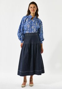 Niebieska bluzka w kwiatowy wzór z bufiastymi rękawami, zestawiona z ciemnoniebieską, warstwową maxi spódnicą o dopasowanej talii i białym przeszyciu.