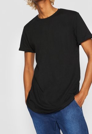 Czarna bawełniana koszulka z krótkim rękawem i okrągłym dekoltem, o luźnym kroju i gładkiej fakturze. Nosi się ją z niebieskimi dżinsami.