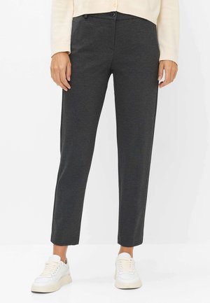 Frau trägt dunkelgraue gerade geschnittene Hose, weiße Sneakers und einen hellbeigen Pullover, ab Taille abwärts gezeigt.