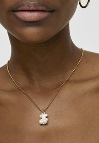Collier en chaîne dorée avec un pendentif en forme d'ours blanc. Texture lisse avec une finition polie. Design simple et ludique.
