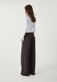 Pantaloni larghi marroni scuri con vita regolabile, due tasche posteriori e una striscia laterale bianca, abbinati a un top bianco aderente.