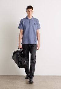Polo shirt bleu, jeans noirs, sac noir et chaussures. La chemise a un col et un logo. Le matériau semble doux, avec une texture lisse.