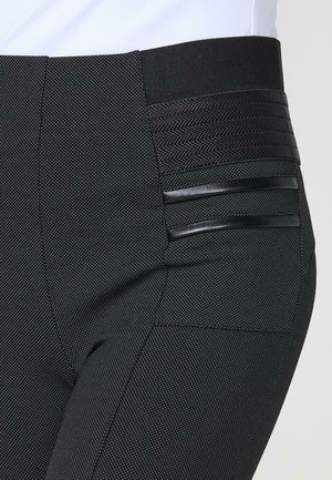 Pantaloni negri dintr-un material texturat, cu un model subtil de puncte; talie lată cu accente țesute și două dungi negre elegante pe laterale.
