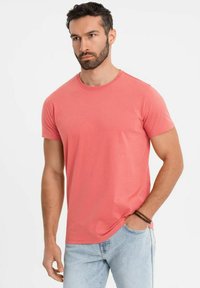 Korálové tričko s krátkým rukávem z měkké bavlny, kulatým výstřihem a volným střihem. V kombinaci se světle modrými džíny.