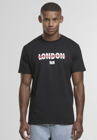 Zwart katoenen T-shirt met vetgedrukte witte tekst "LONDEN" met rode accenten. Ronde halslijn, korte mouwen en een standaard pasvorm. Casual stijl.