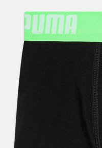 Sous-vêtements de sport noirs avec une ceinture élastique vert clair portant le texte "PUMA". Le matériau semble lisse avec des détails de couture fins.