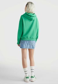 Sudadera verde con capucha, mangas largas y corte holgado, combinada con una falda de mezclilla azul claro. Medias blancas hasta la rodilla y zapatillas verdes.