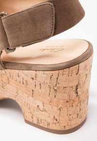 Sandale à semelle compensée en daim marron avec bride de cheville ajustable et semelle plateforme en liège, mettant en valeur le matériau texturé et les détails cousus.