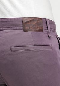 Fioletowe bawełniane spodnie z tylną kieszenią oraz brązową skórzaną metką z wytłoczonym napisem "BOSS ORANGE". Gładka tekstura i dopasowany kroj.