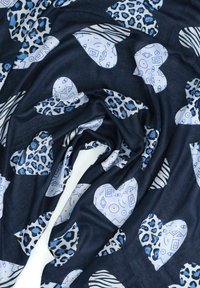 Tessuto scuro con forme a cuore blu e bianche, caratterizzato da motivi astratti geometrici e a stampa animale, disposti con pieghe morbide.