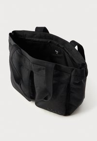 Sac fourre-tout noir en matériau lisse et texturé. Dispose de deux poignées, d'un intérieur spacieux et d'un logo embossé sur le côté.